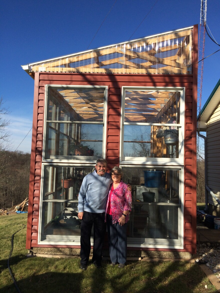 Larry and Susan Dale stand in front of the greenhouse they built atop a cistern that collects rain water. The DuPont landfill begins on the ridge directly behind them. They say they live in the shadow of DuPont, and if the shadow had a shape, it would be