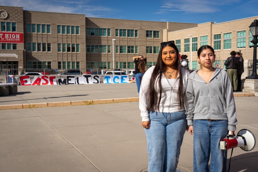 East High School senior Leslie Hernandez and junior Natasha Gonzalez stand in front of their school and signs that spell out “EAST MELTS ICE,” Feb. 6, 2026. The two students helped organize the Friday student protest against federal immigration enforcement.