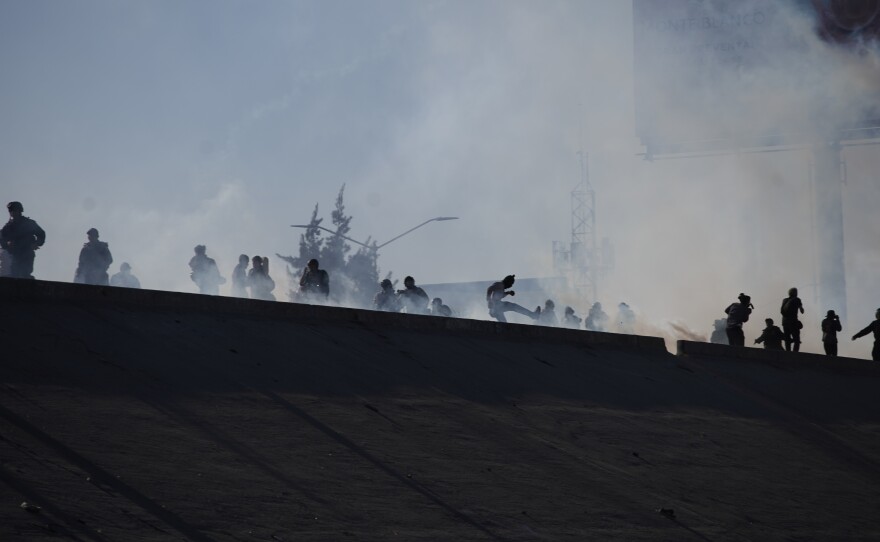 Migrants run from tear gas launched by U.S. agents, amid members of the press, at the top of a riverbank at the Mexico-U.S. border after a group of migrants pushed past Mexican police at the Chaparral crossing in Tijuana, Mexico, Sunday, Nov. 25, 2018. 