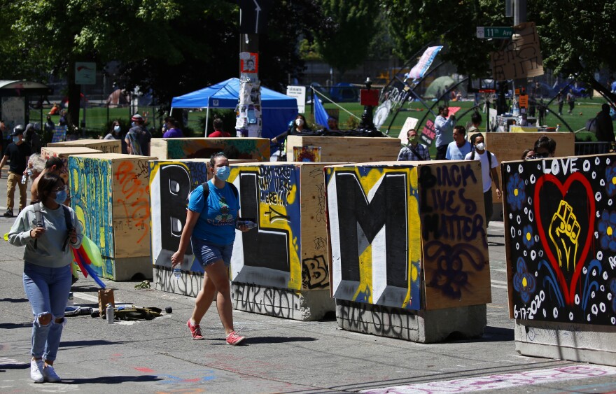 People walk around new concrete barricades topped with plywood that were installed by city workers. To the city, the new barriers open access for local traffic, but protesters believe the move shrinks their protest space.