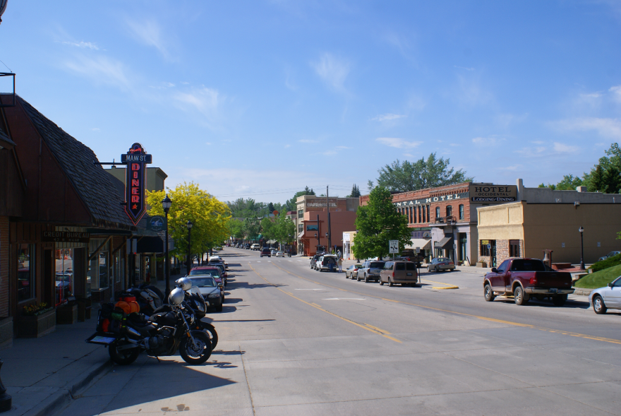 A two-way street in a small area. There's a diner on one side of the road and a hotel on the other, with cars parked along the side of the road.