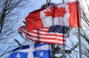 Flags for Vermont, Canada and Quebec fly against bare winter trees and a blue sky.