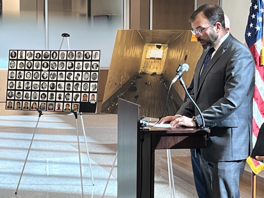 Justin Simmons, U.S. Attorney for the Western District Court of Texas, speaks about the criminal charges and sentencing of Rigoberto Miranda-Orozco next to a government exhibit showing the inside of the tractor-trailer involved in the smuggling operation and photos of the 53 people who died, and 11 who were injured.