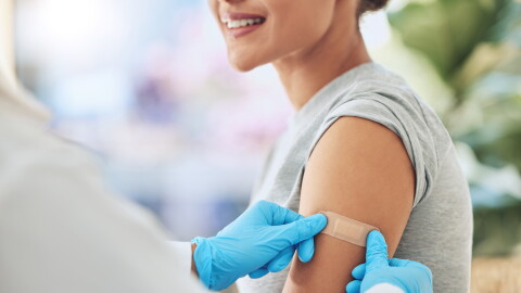 Band aid, vaccine or injection for covid and global virus in security, safety or wellness insurance. Doctor hands, medical employee or healthcare worker with plaster for happy or smile hospital woman.