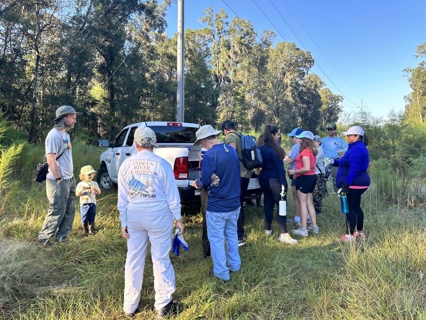 Twelve volunteers gather by Environmental Specialist Jesse Natwick’s truck before heading into the woods to pull invasive coral ardisia. (Chloe Knowles/WUFT News)