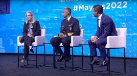 Reno Mayor Hillary Schieve is sitting on-stage at the United States Conference of Mayors. She is speaking to an audience out of frame. To her right sit U.S. Surgeon General Dr. Vivek Murthy and Miami Mayor Francis Suarez, listening intently. 