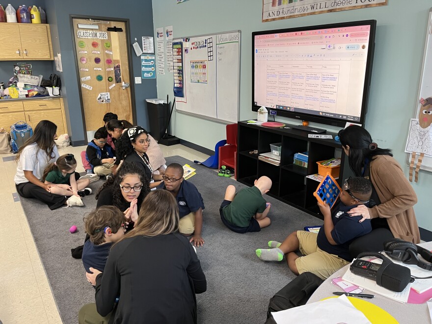 Women and children sitting together on the rug in a classroom.