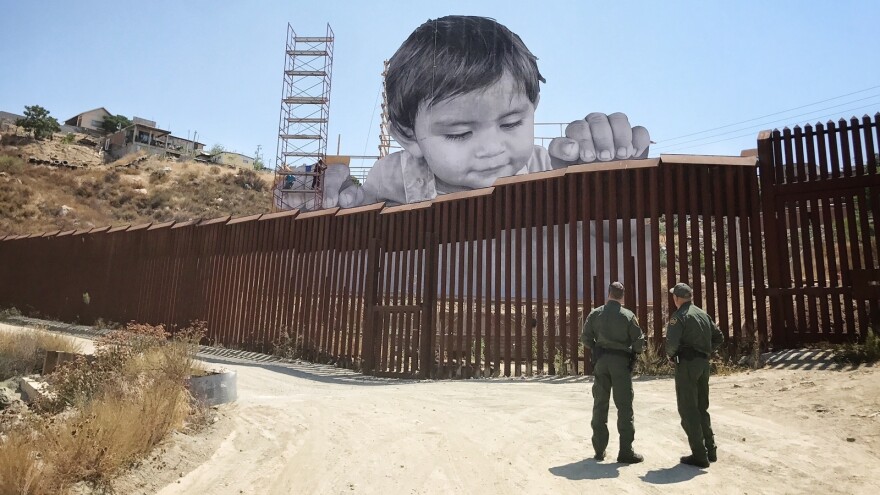 The boy glances down from the Mexican side at two Border Patrol officers, who return his stare from the U.S.