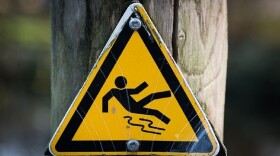 A yellow warning triangle sign showing a person slipping on the ground.