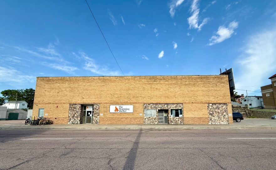A brick builing that looks like it was built in the 1970s has a sign that says "warming shelter."