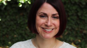 a woman with short, dark hair with a reddish tone, smiles in front of an ivy background