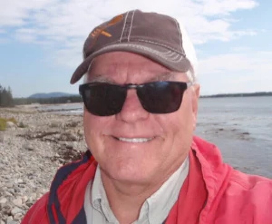 A man wearing sunglasses smiles into the camera