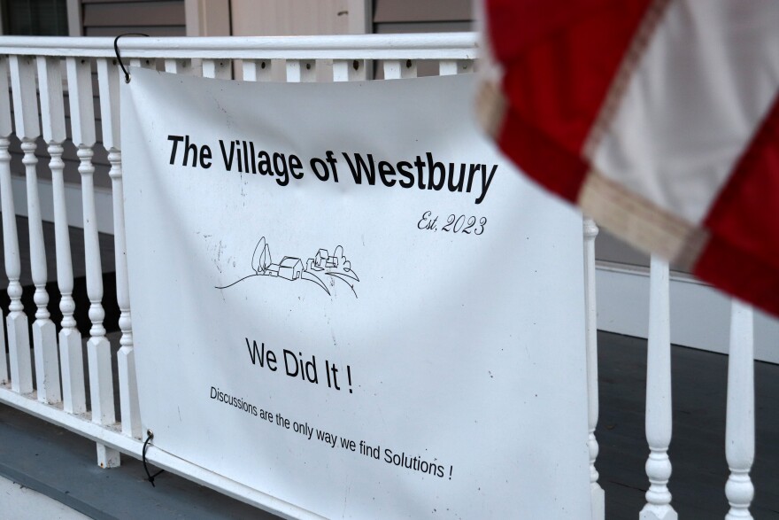 A sign reads "the village of Westbury, est. 2023, we did it! Discussions are the only way we find solutions!"