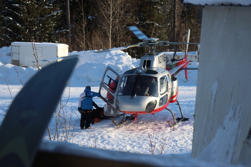 A red-and-silver helicopter on the ground with people around it. The blades are still rotating.
