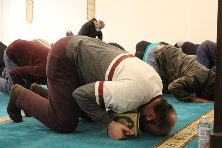 A man holding a book touches his head to the carpet