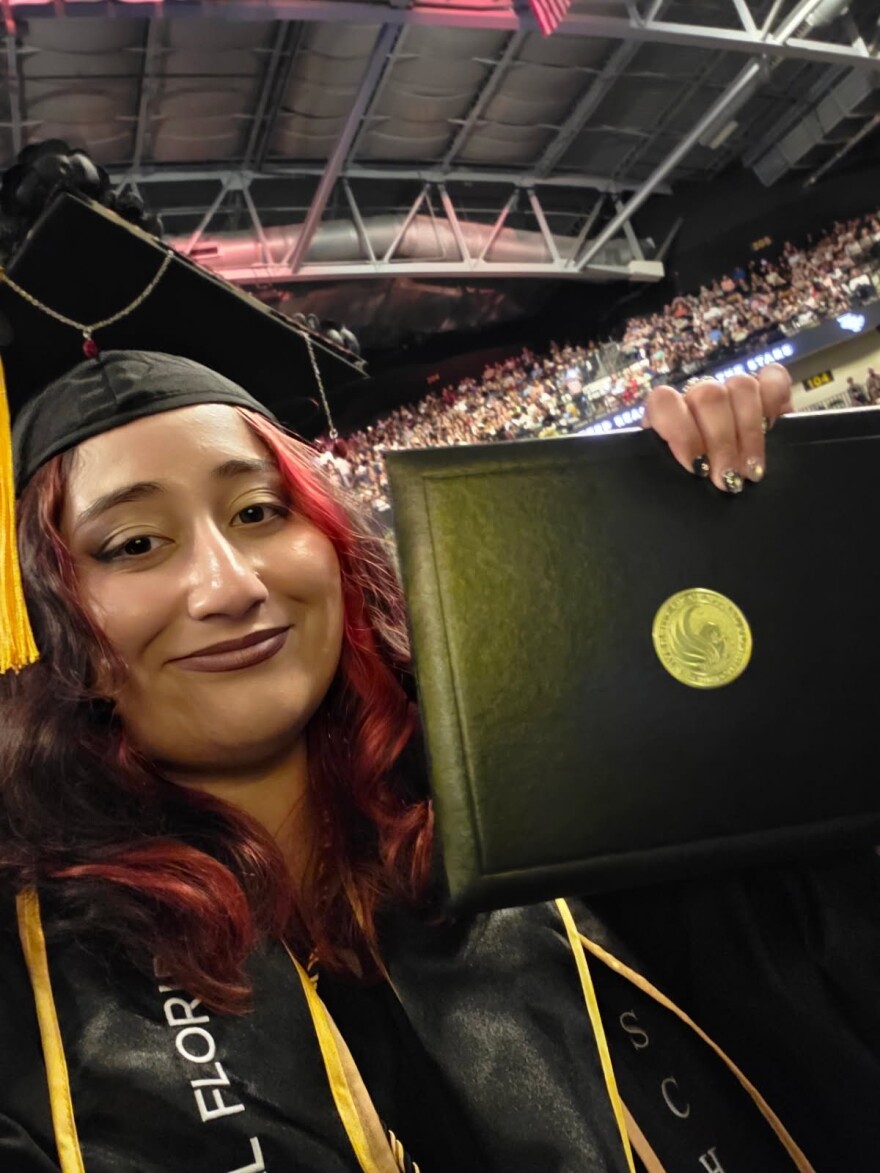 A college graduate smiles in a selfie taken while holding her degree during her UCF commencement ceremony. 
