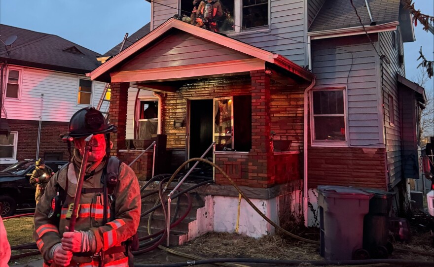 An unnamed firefighter stands before a burnt house.