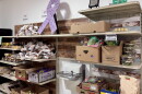 Boxes of vegetables and berries, bags of potatoes and containers of bakery items sit on shelves in a lit room.