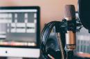 A grey microphone with headphones hung on it in front of a blurry background.