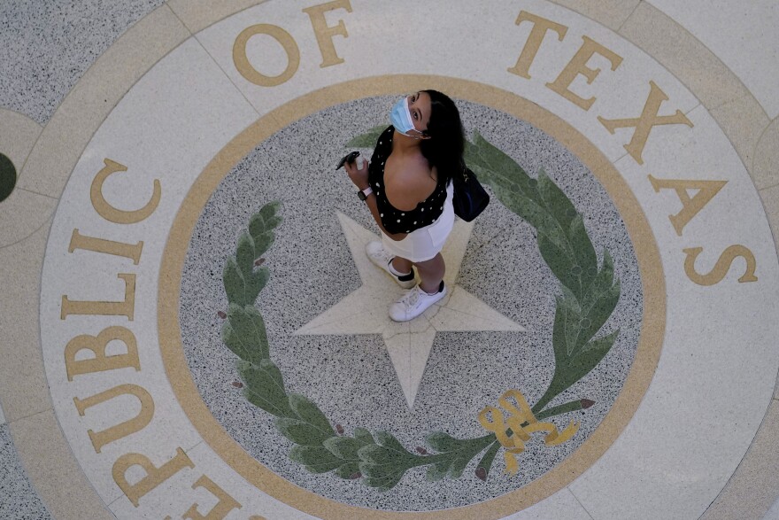 Photo from above of a woman wearing a mask standing in the center of the state seal at the Texas State Capitol.