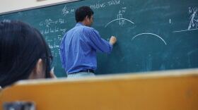 A physics teacher writes on his chalkboard in a classroom. 