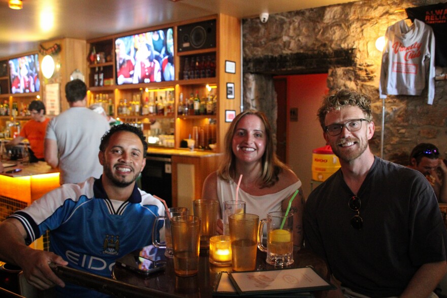 Three friends smile for a photo inside a bar.