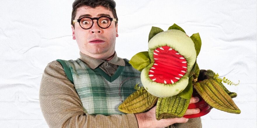 A person in glasses looking shocked with a plant puppet in one hand