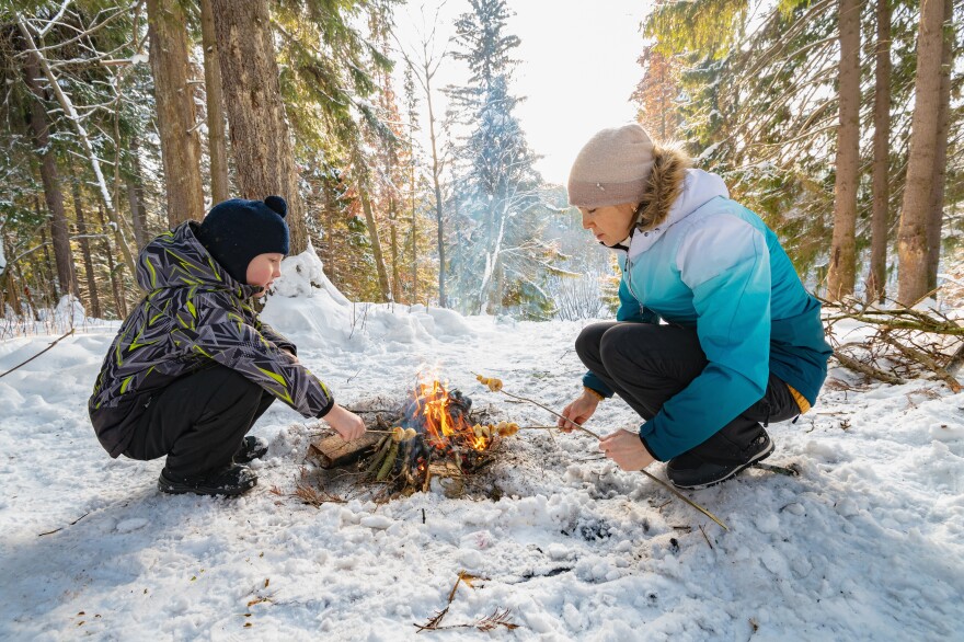 A woman and a boy around a campfire in winter in the forest fry dumplings on skewers.