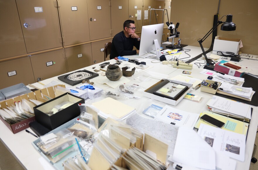 Jamie Jacobs of the Tonawanda Seneca Nation, Turtle Clan, and curator at the Rochester Museum and Science Center for the Rock Foundation works on cataloging Seneca artifacts for an exhibition at the Heard Museum . Jacobs has been linking Seneca art and artifacts to the language through an eighteenth century Jesuit translation of Seneca he references on his iPad.