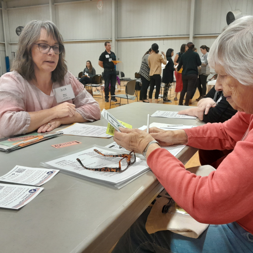 Two women seated at a table consulting a pile of papers