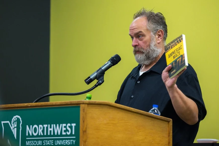 Fiction writer Michael Czyzniejewski presents his book, “The Amnesiac in the Maze,” for sale at the Visiting Writers Series Nov. 13. The event hosted two writers presenting passages to students interested in writing.