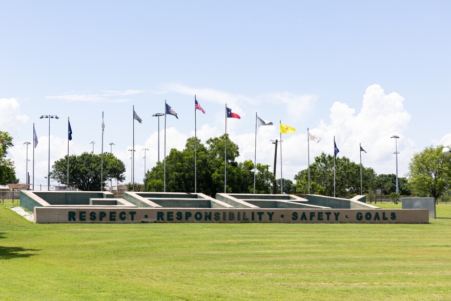 A sign near the entrance of Gary Job Corps Center in San Marcos reading the words respect, responsibility, safety and goals with flags flying behind with another sign reading GARY. 