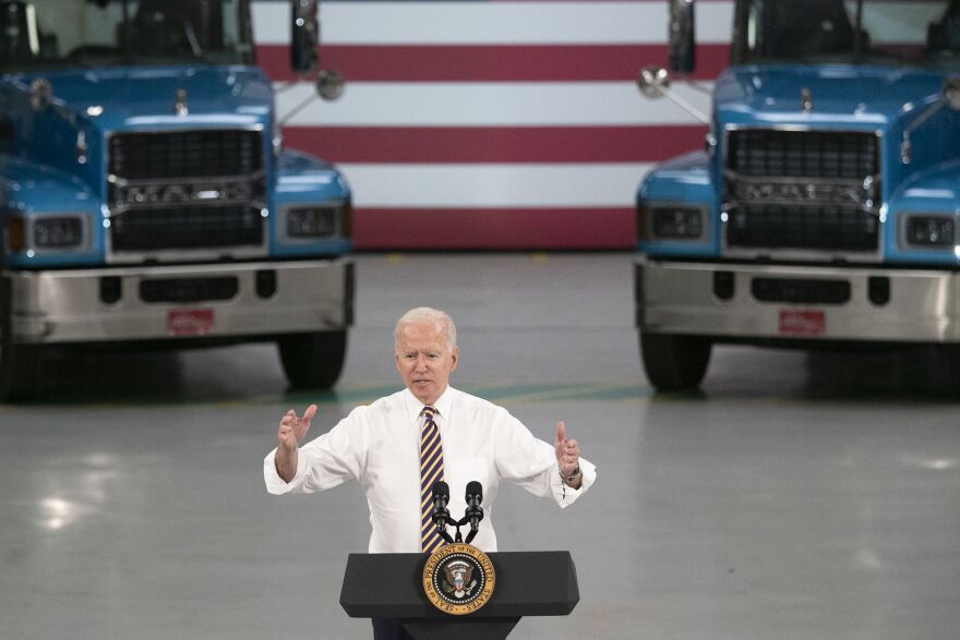 Joe Biden speaking at a podium in front of two trucks