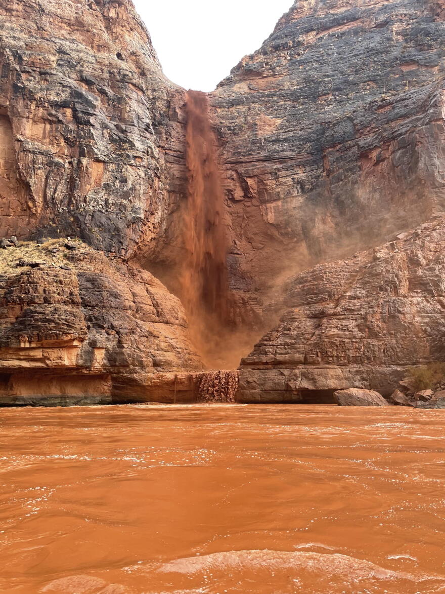 A rust-colored waterfall spills over desert rock