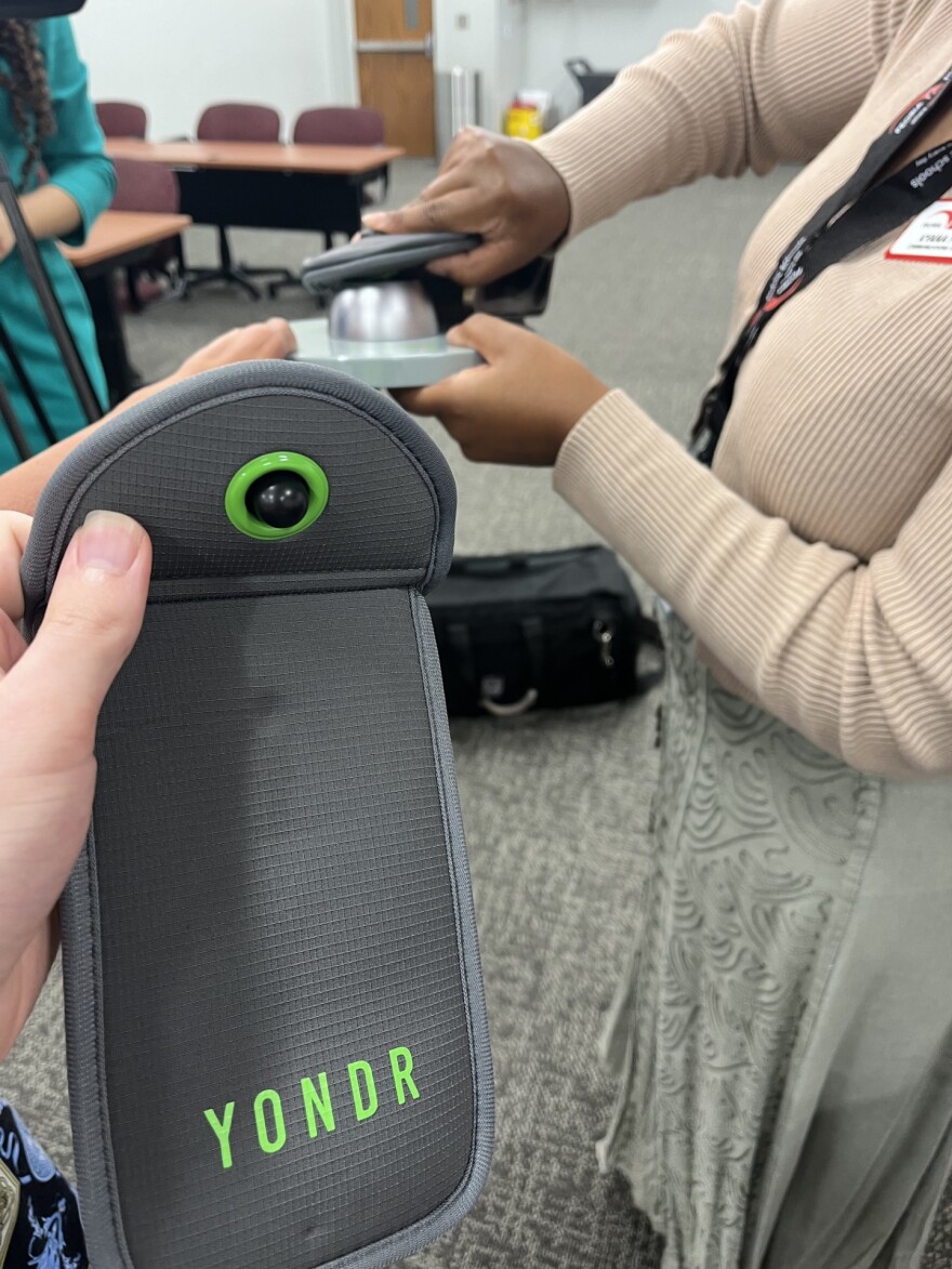 A look at the grey and green Yondr pouches, and the magnetic base that unlocks them in the background. The pouches also have a slot for an identification card on the back, so students can track down lost pouches easily.