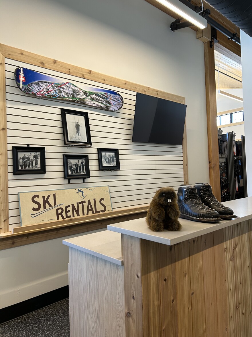 A beaver stuffed animal sits on a desk in front of a sign that says "ski rentals" and a snowboard 