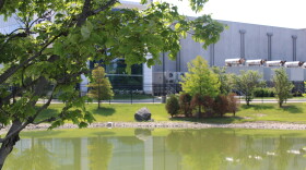 A photo of a pond in front of a data center fenced off behind it, a tree is close to the screen. 