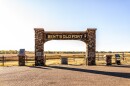 This is an image of a gated entrance with a large sign that says "Bent's Old Fort" on a clear-sky day. 
