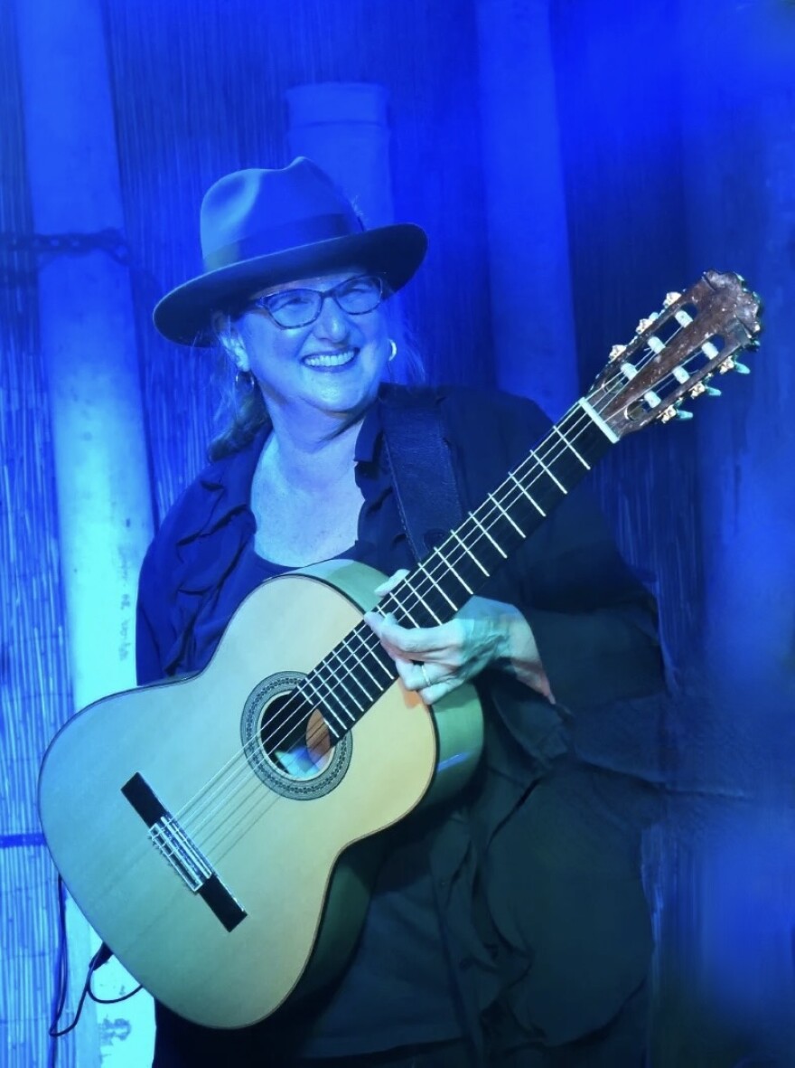 A woman on a blue lit stage performing with an acoustic guitar. 