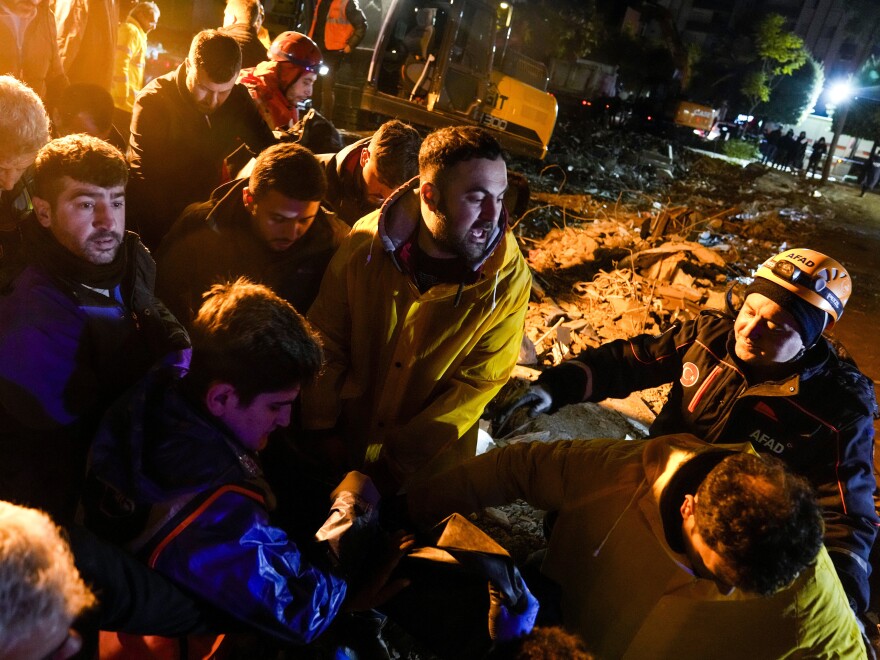 Emergency team members carry the body of a person found in the rubble of a destroyed building in Adana, Turkey, on Monday.