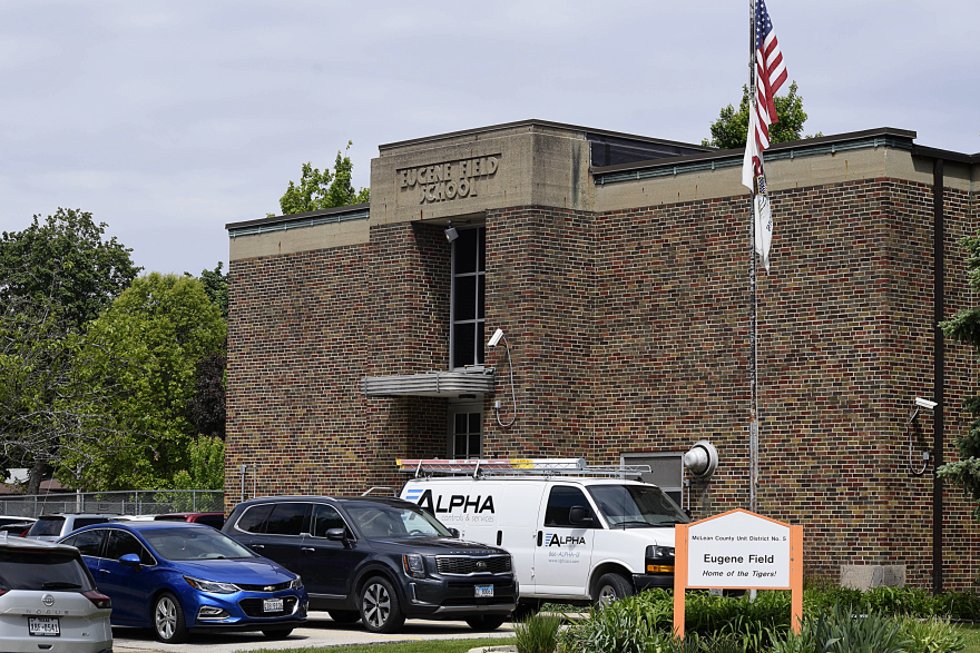 A view of a brick building from the outside. Cars are parked out front.