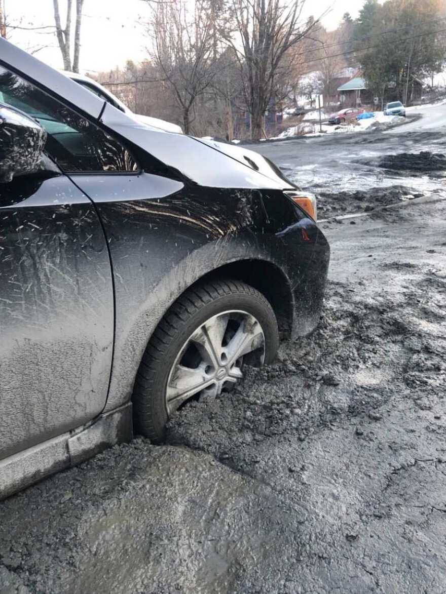 A grey car with a black tire is submerged in mud 