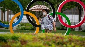 A woman holds an umbrella walking past the Olympic Rings in front of Japan Olympic Museum in Tokyo.