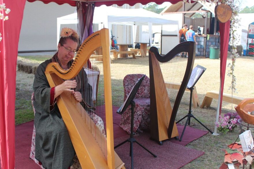 Teresa Songster, 50, strums a soft melody on her harp next to an empty chair waiting to be filled by her daughter, Heather. Songster started playing the harp in 2000, after her daughter took an interest, and has been playing at Hoggetowne ever since. The mother-daughter pair from Orlando call themselves the Harpies.(Teal Garth/WUFT News)