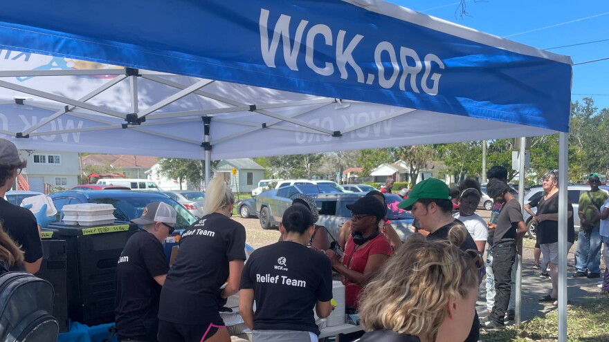 People under a tent serving food to people standing in line