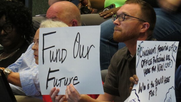 A man holds a sign that reads "Fund Our Future" at a Cincinnati School Board meeting. 
