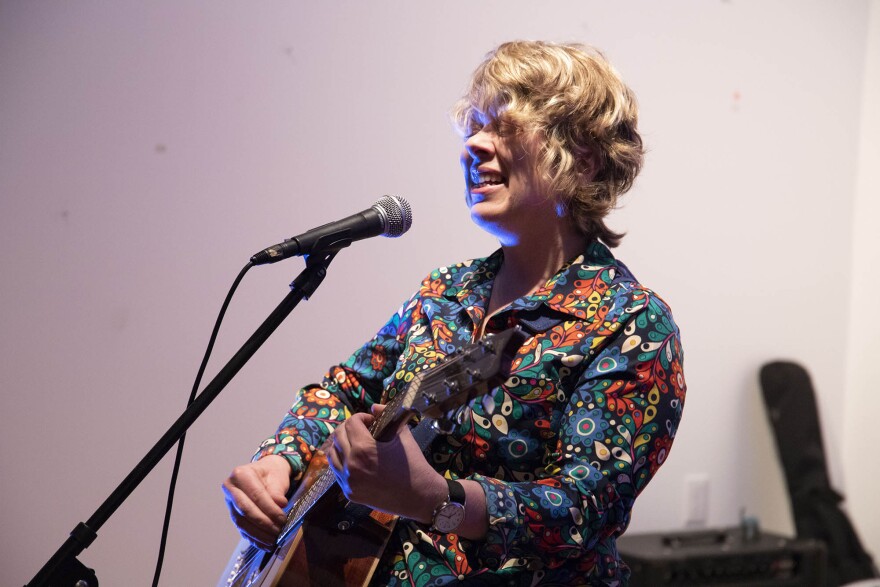 Woman singing into a microphone and playing guitar