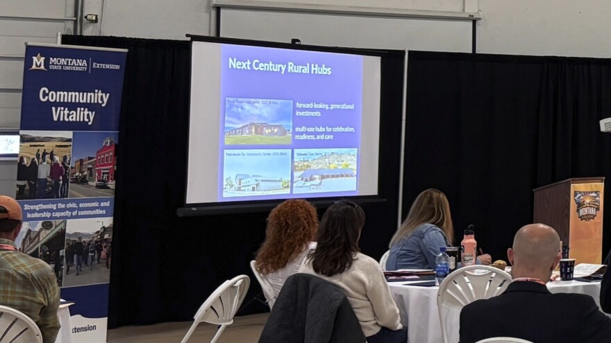 Attendees watch a presentation titled “Next Century Rural Hubs” during Montana State University’s Rural Summit. A Montana State University Extension banner stands beside the projection screen. 