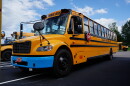 Yellow school bus with blue bumper sits in bus parking lot.