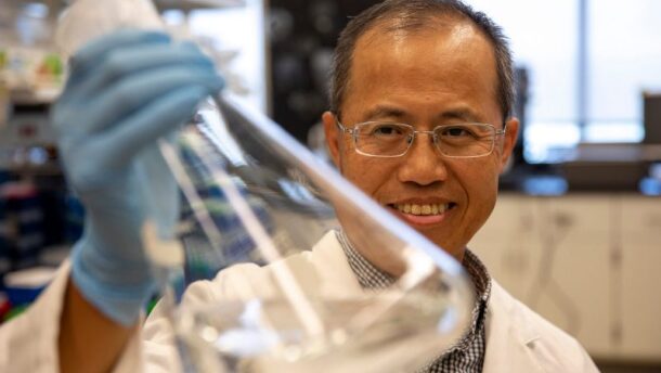 A man wearing glasses holds a beaker inside a laboratory.